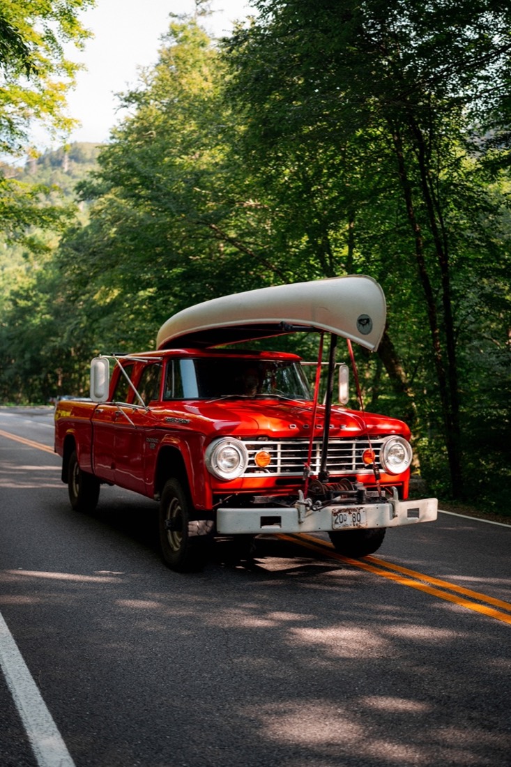 Classic red pickup with a canoe on top, parked on a wooded road